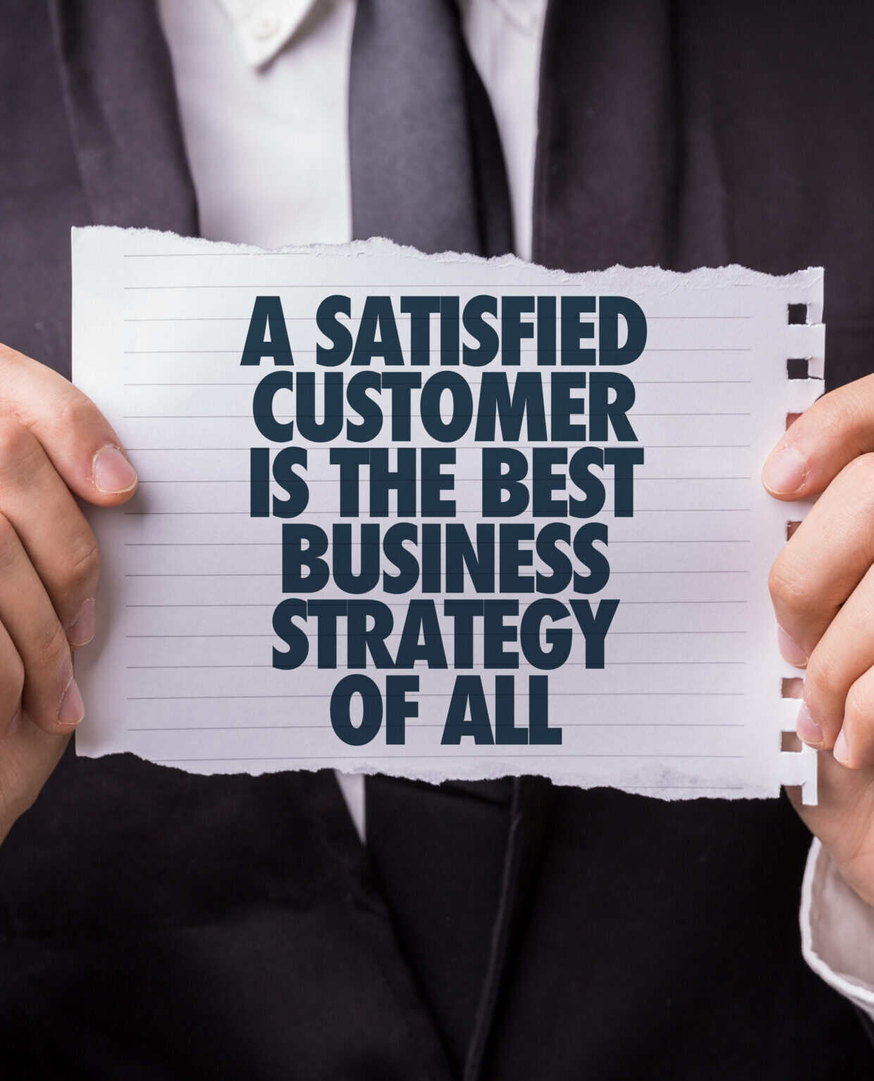 A person in a suit holds a piece of lined paper with the words "A satisfied customer is the best business strategy of all" printed in bold, dark letters—highlighting the importance of positive reviews for Google My Business.