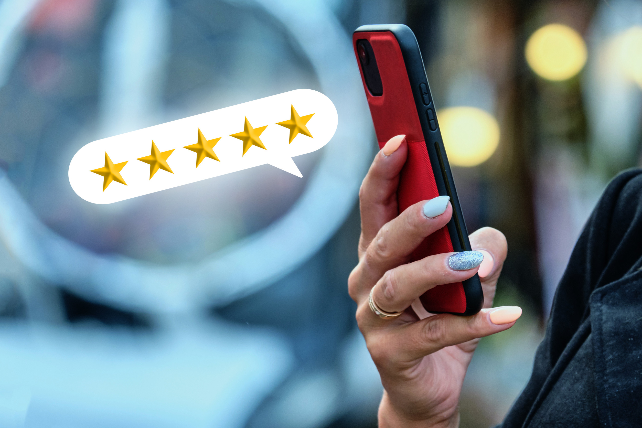 A person holding a red smartphone with a speech bubble showing five gold stars, indicating recent customer feedback or high rating. The background is blurred and the person has multicolored nails.