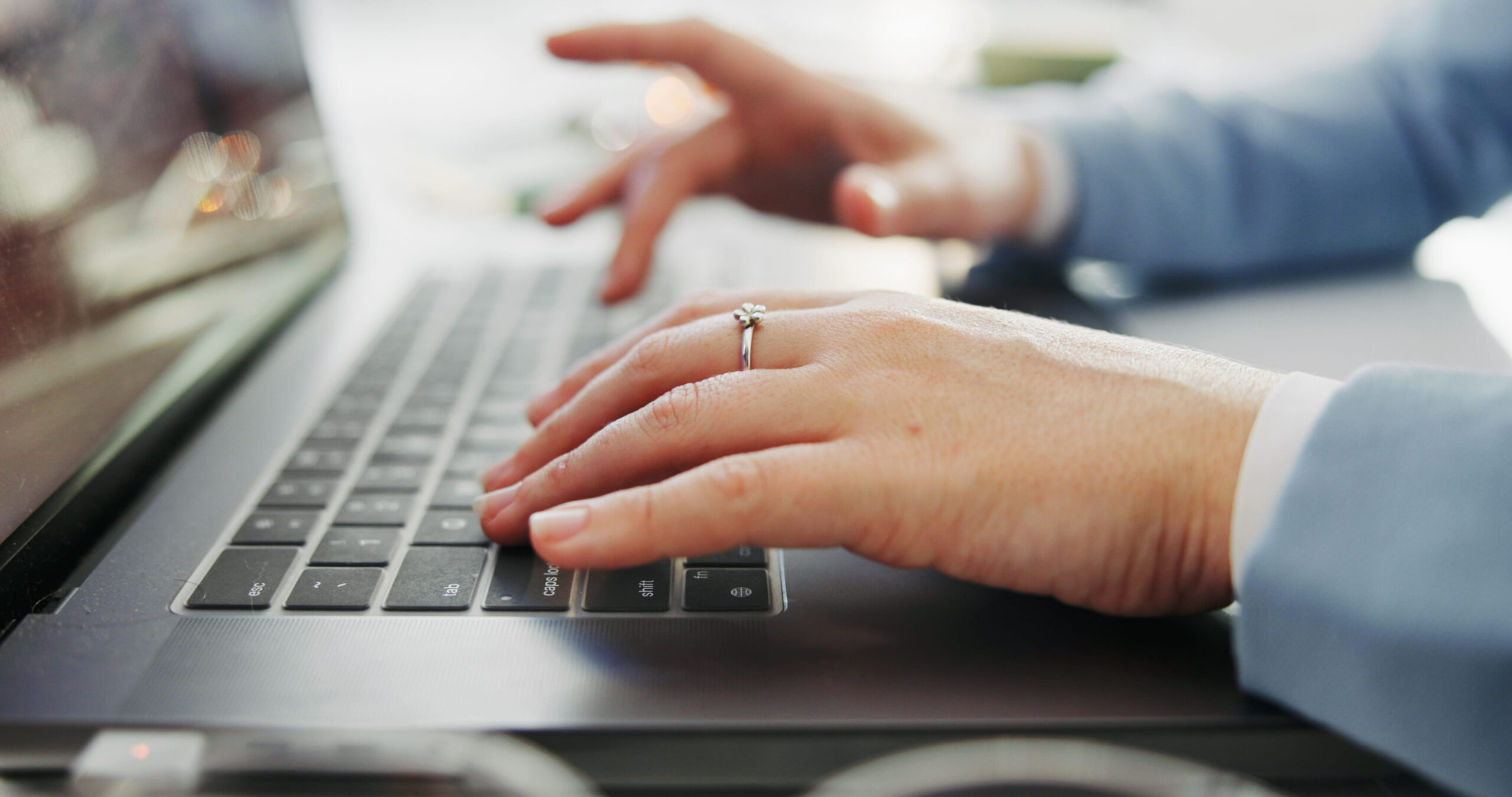 Close-up of a person’s hands typing on a laptop keyboard, focusing on a ring worn on the left hand. The light blue sleeve suggests professionalism, ideal for tasks like review generation to boost SEO and build consistent reviews online.